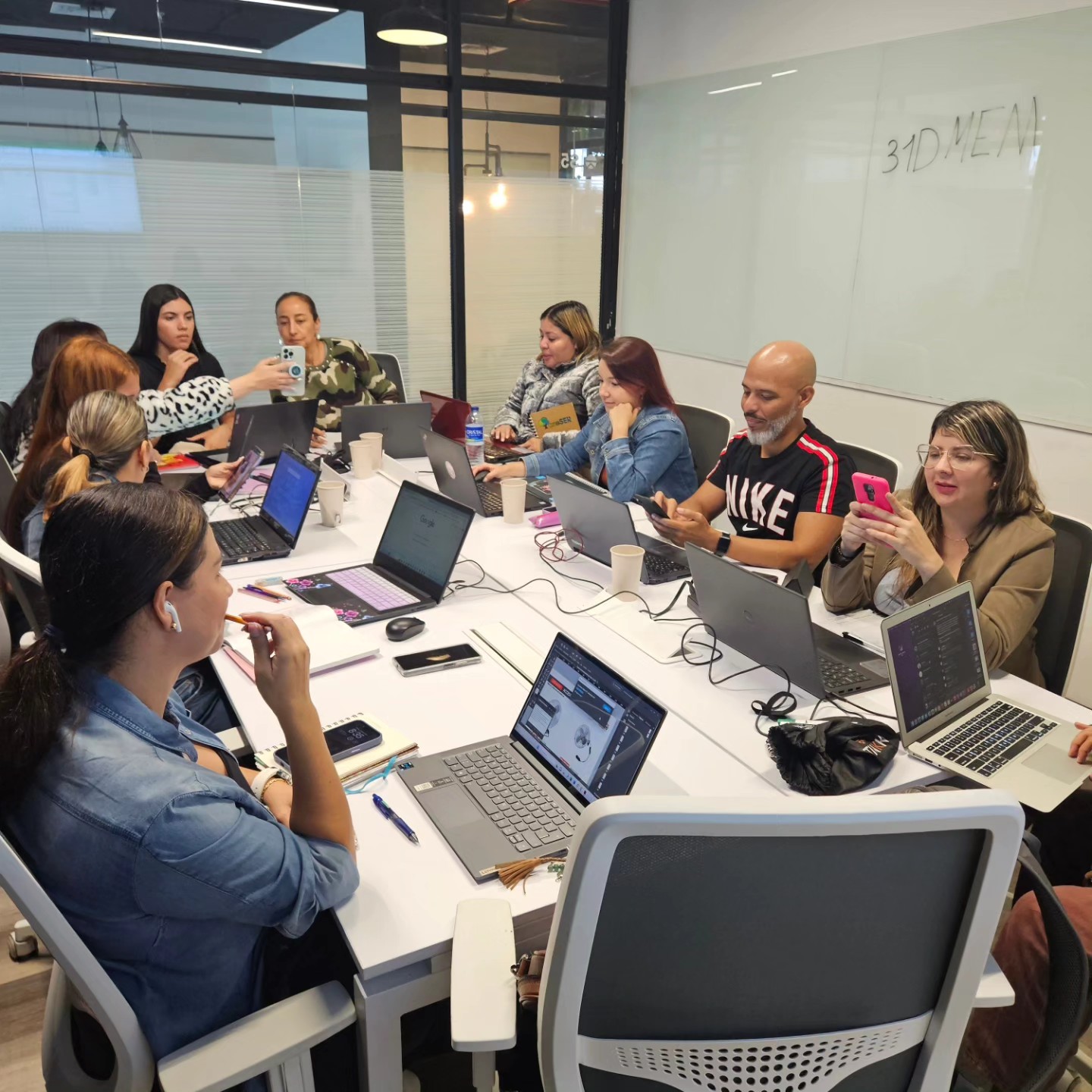 Grupo de estudiantes en aula presencial con laptops, aprendiendo marketing digital con IA